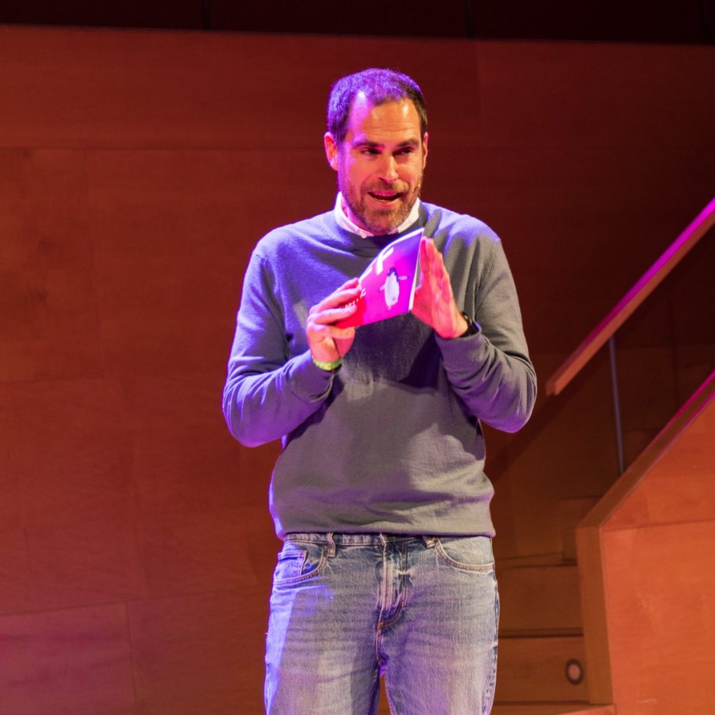 Joan Martín hablando en un escenario, con un programa en las manos